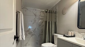 Un baño con inodoro, lavabo, ducha con puerta de vidrio y toallero.