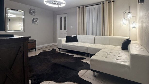 Una sala moderna con un sofá modular, un tapete oscuro, un ventilador de techo e iluminación empotrada.