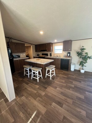A compact kitchen with wooden cabinets, a central island with stools, a microwave, and a sink. - 5-bdr 3 bath fully furnished house in Burnside Ky minutes from Lake Cumberland (Burnside)