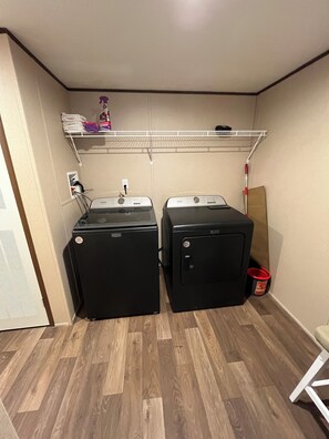 A laundry room with two front-loading washers and dryers, a metal shelf above, and a white chair to the right. - 5-bdr 3 bath fully furnished house in Burnside Ky minutes from Lake Cumberland (Burnside)