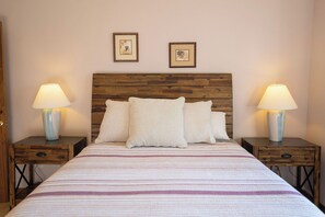 Een bed met een houten hoofdeinde, twee nachtkastjes met lampen, en twee ingelijste foto's aan de muur.