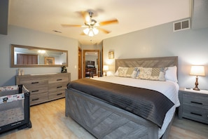 A bedroom with a bed, bedside tables, a dresser, a ceiling fan, and a mirror.