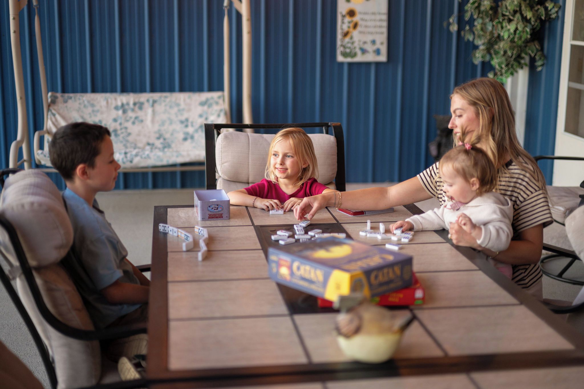 A family playing board games at a table with a blue wall and a plant in the background.