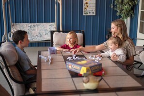 A family playing board games at a table with a blue wall and a plant in the background.