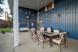 An outdoor patio with a blue wall, a dining table with chairs, string lights, and a clock.