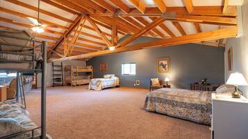 A spacious attic bedroom with a high ceiling, wooden beams, bunk beds, a desk, and a chair.