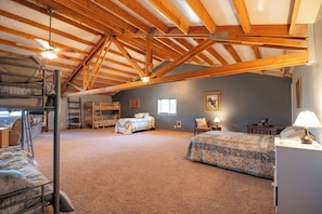 A spacious attic bedroom with a high ceiling, wooden beams, bunk beds, a desk, and a chair.