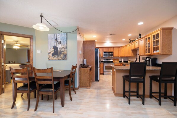 A modern kitchen with wooden cabinets, a dining area with wooden chairs, and a painting on the wall.