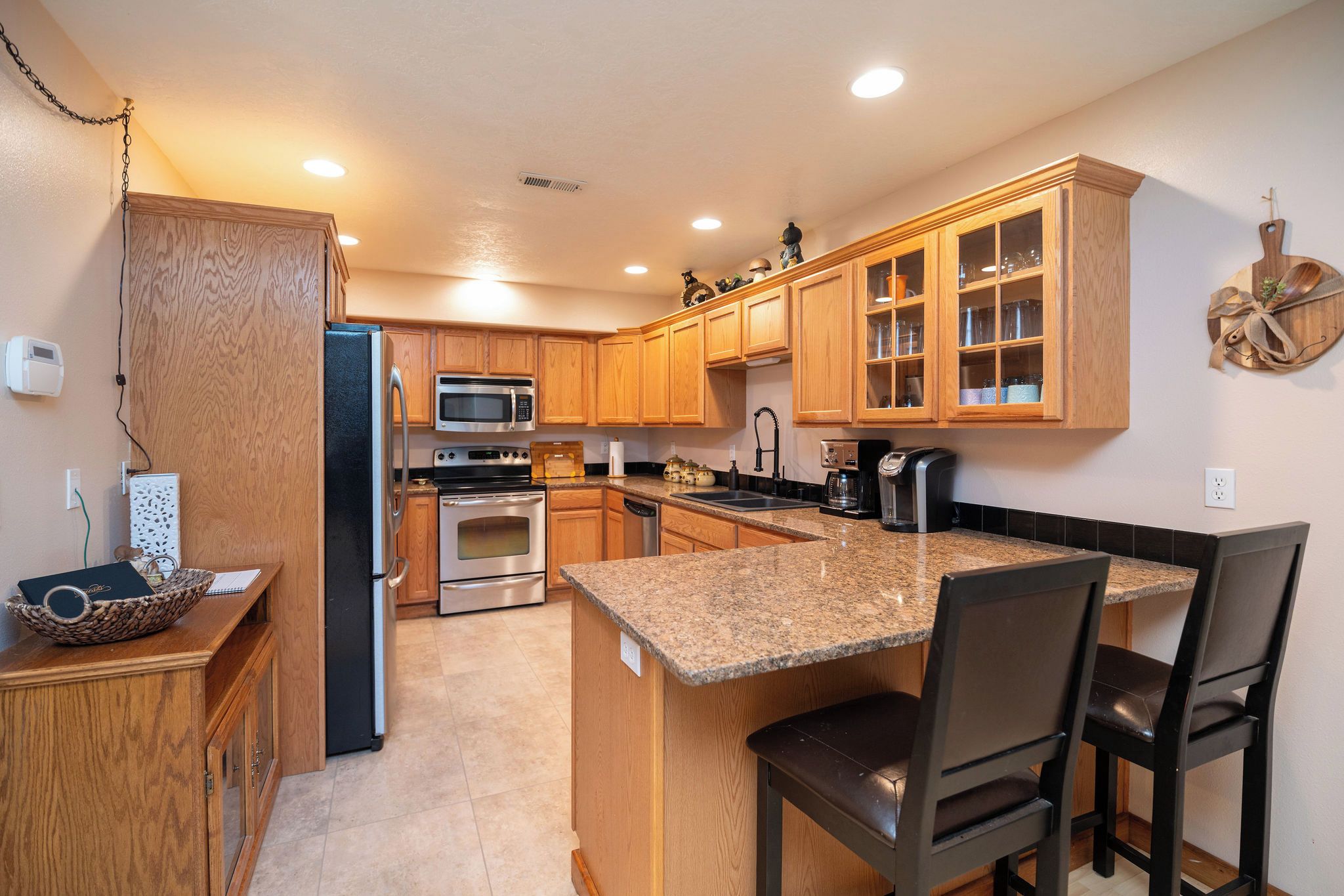A kitchen with wooden cabinets, a granite countertop, stainless steel appliances, and a breakfast bar with chairs.