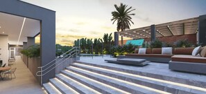 A modern outdoor area with a staircase leading to a seating area, surrounded by greenery and a sunset view.