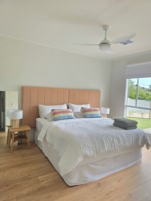 A bedroom with a large bed, a ceiling fan, and a view of the outdoors.
