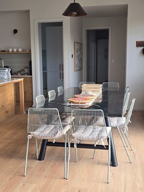 Uma área de refeições com mesa preta, cadeiras de arame branco e piso de madeira.