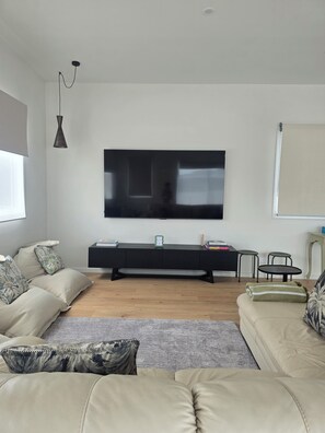 A modern living room with a large flat-screen TV mounted on the wall, a black entertainment unit, a beige sofa, and a patterned rug.