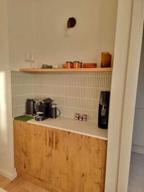 A kitchenette with a coffee maker, kettle, and tea kettle on the counter.