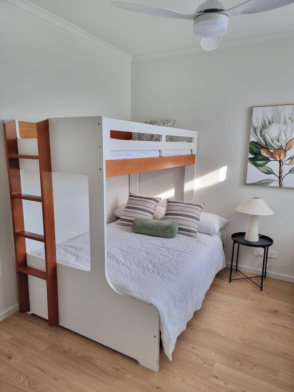 A bunk bed with a wooden ladder, a bedside table with a lamp, and a wall-mounted ceiling fan.