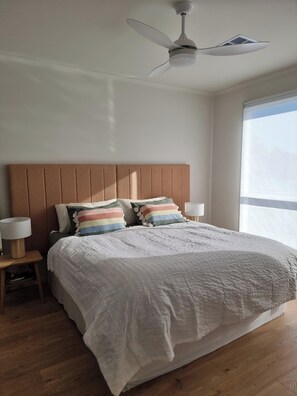 Quarto com cama, duas luminárias de cabeceira, ventilador de teto e janela.
