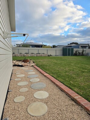 A residential backyard with a gravel pathway, a green lawn, and a metal fence.