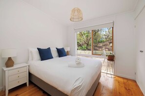 Ein Schlafzimmer mit Bett, Nachttisch, Lampe und Blick ins Freie durch ein großes Fenster.