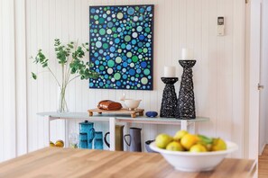 A dining area with a table, a bowl of fruit, a vase with greenery, a decorative painting, and a wall-mounted thermostat. - Harbour Grove Blairgowrie Coastal Sanctuary (Blairgowrie)