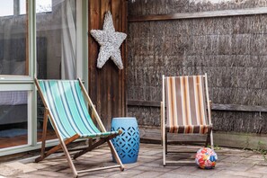 Zwei gestreifte Lounge-Stühle und ein farbenfroher Ball auf einer gepflasterten Terrasse mit Holzzaun und einer Sternen-Dekoration.