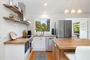 A modern kitchen with white cabinetry, wooden countertops, a built-in oven, a dishwasher, and a large window offering a view of greenery. - Harbour Grove Blairgowrie Coastal Sanctuary (Blairgowrie)