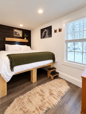 A bedroom with a bed, a wooden headboard, a window with a view, and a fluffy rug. - Vermont Group Getaway. Hot Tub, Game Room & Reservoir Views. Near Mt Snow (Whitingham)
