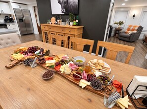 A dining area with a wooden table set for a meal, featuring a variety of cheeses, meats, and fruits. - Vermont Group Getaway. Hot Tub, Game Room & Reservoir Views. Near Mt Snow (Whitingham)
