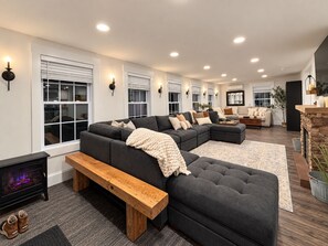 A modern living room with a sectional sofa, a wooden bench, and a fireplace. - Vermont Group Getaway. Hot Tub, Game Room & Reservoir Views. Near Mt Snow (Whitingham)