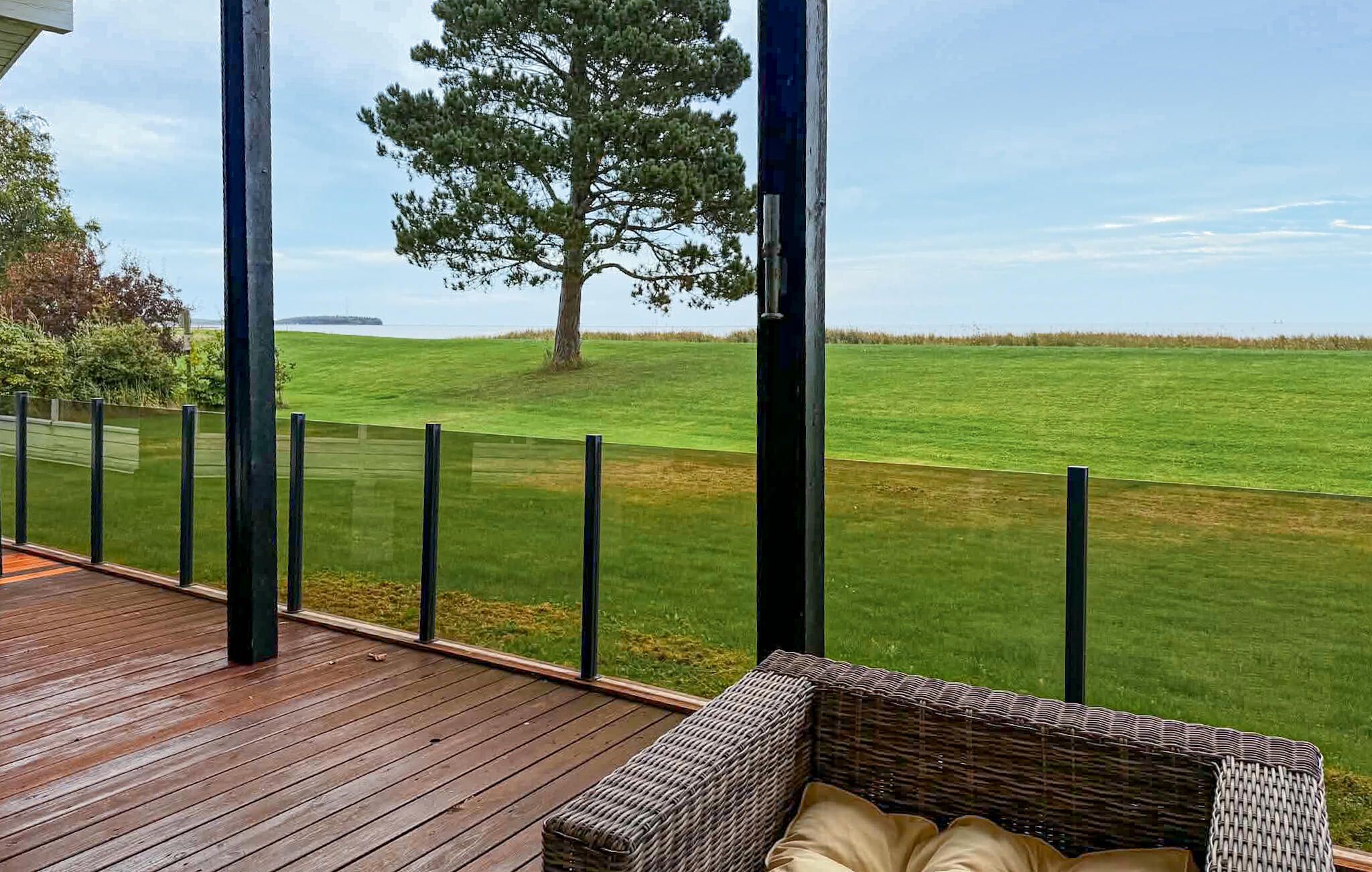 Eine Holzterrasse mit einer Korbsitzgruppe und Blick auf ein grasbewachsenes Feld mit einem Baum.