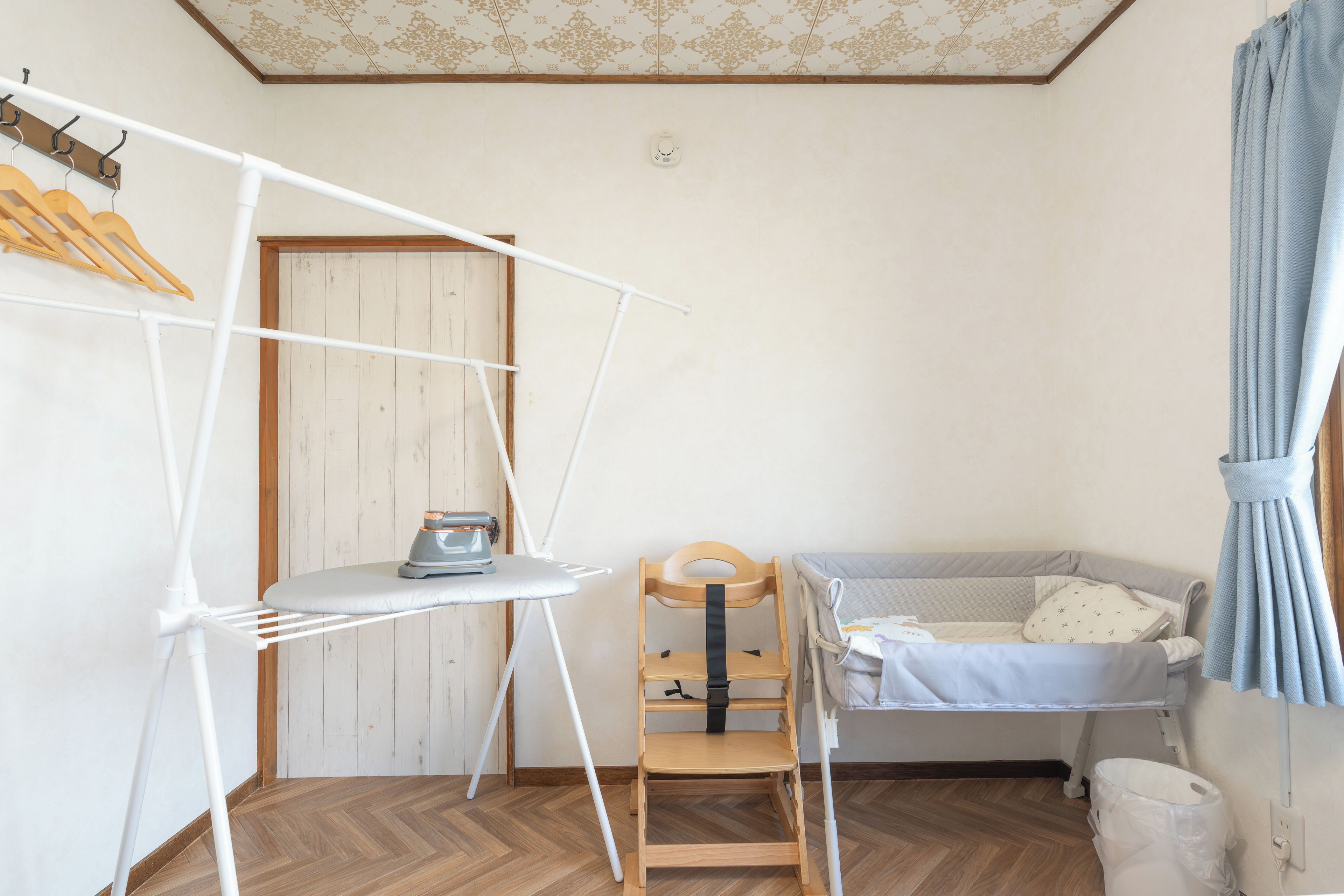 Ein Zimmer mit Holzboden, einem Bett mit weißer Daunendecke, einem Holzstuhl, einem weißen Bügelbrett und einem an der Wand montierten Heizgerät.