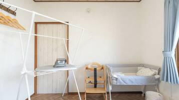 Ein Zimmer mit Holzboden, einem Bett mit weißer Daunendecke, einem Holzstuhl, einem weißen Bügelbrett und einem an der Wand montierten Heizgerät.
