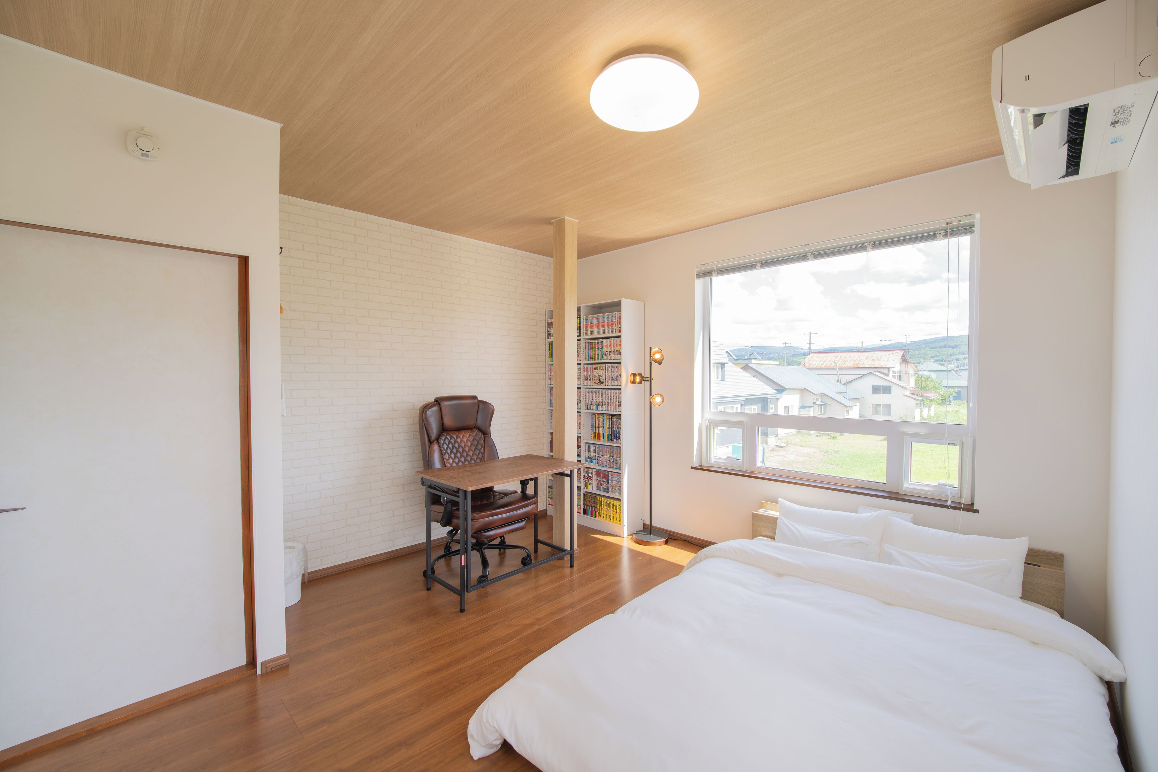 A bedroom with a bed, a desk, a chair, a bookshelf, and a window with a view.