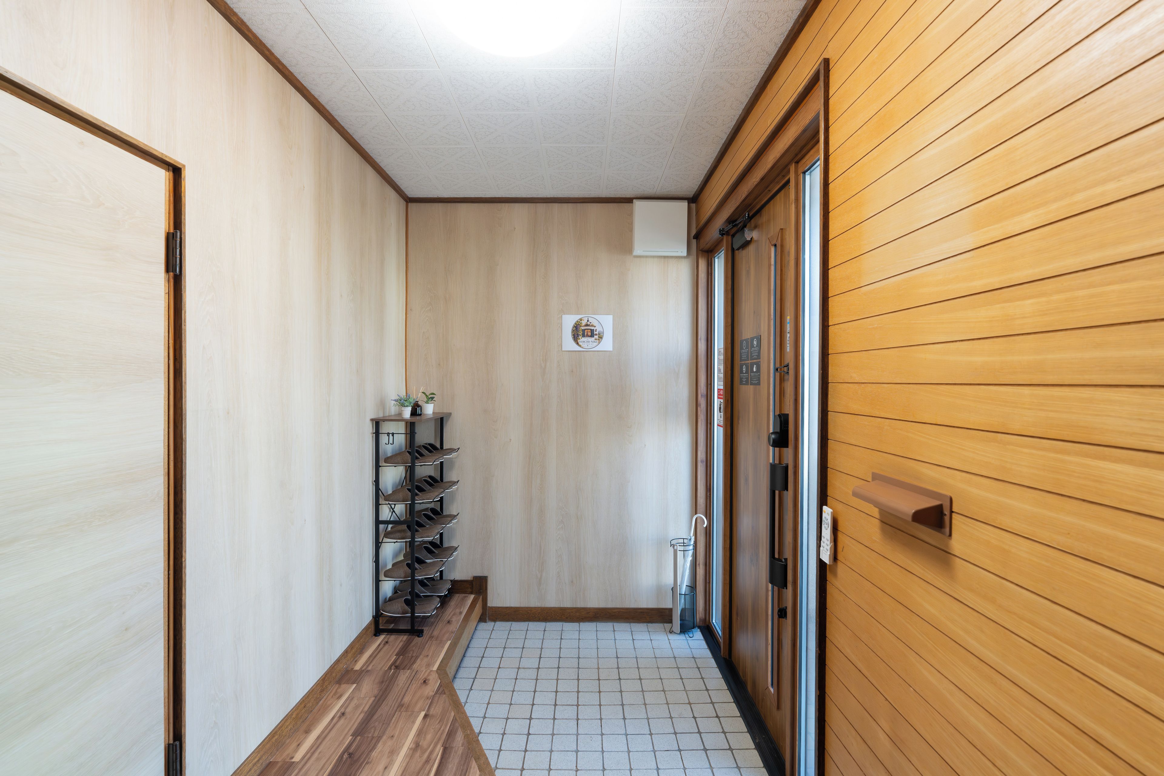 A hallway with wooden walls, a tiled floor, and a shoe rack with shoes.