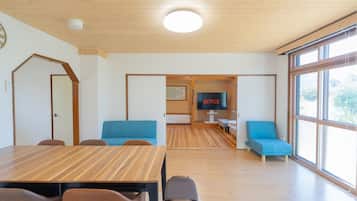 Un interior moderno con suelo de madera, una mesa de comedor, sofás azules y un televisor que muestra 'NETFLIX'.