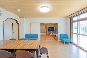 Um interior moderno com piso de madeira, mesa de jantar, sofás azuis e uma televisão exibindo 'NETFLIX'.