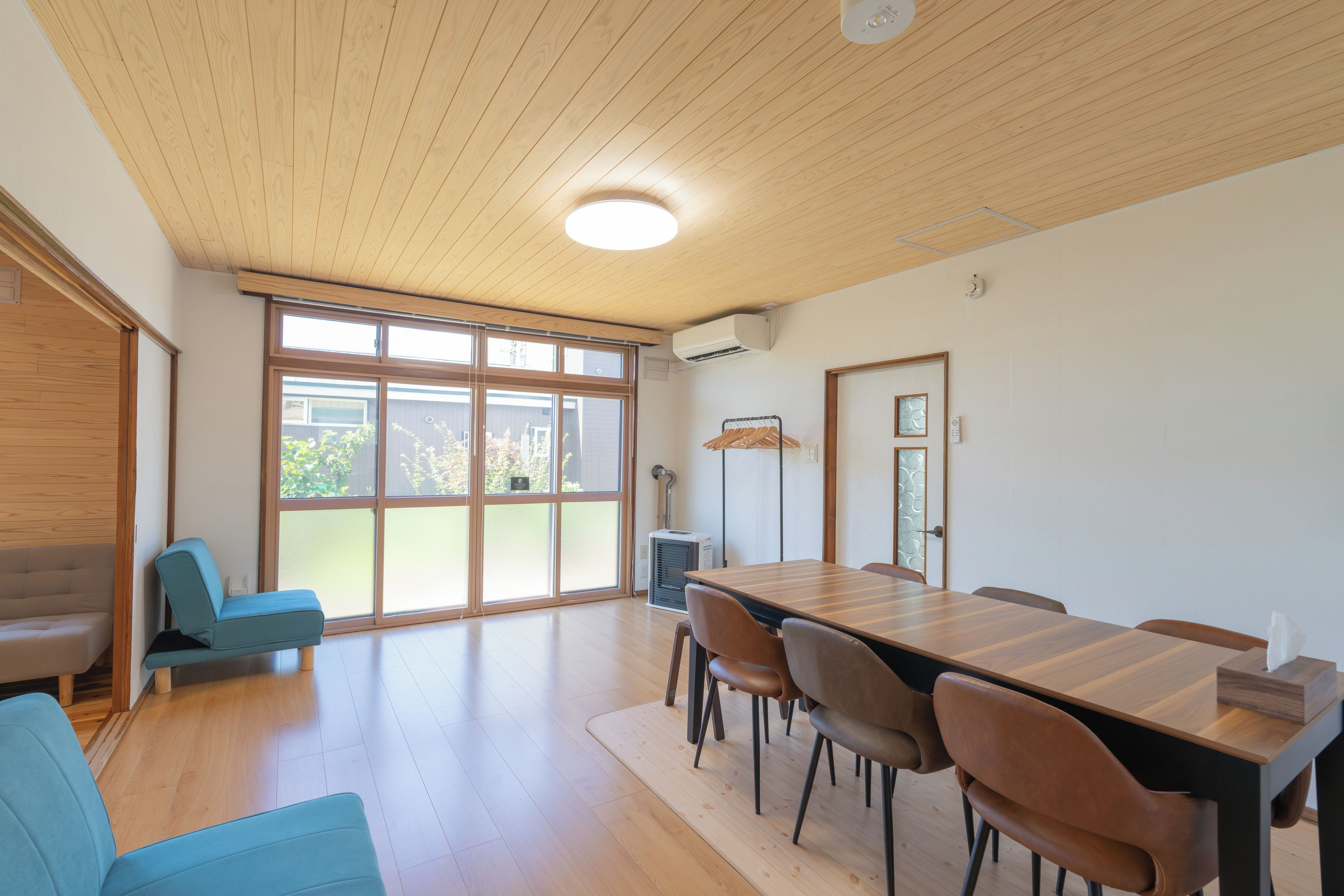A modern interior with a wooden ceiling, a dining area with a table and chairs, and a seating area with a sofa and chairs.