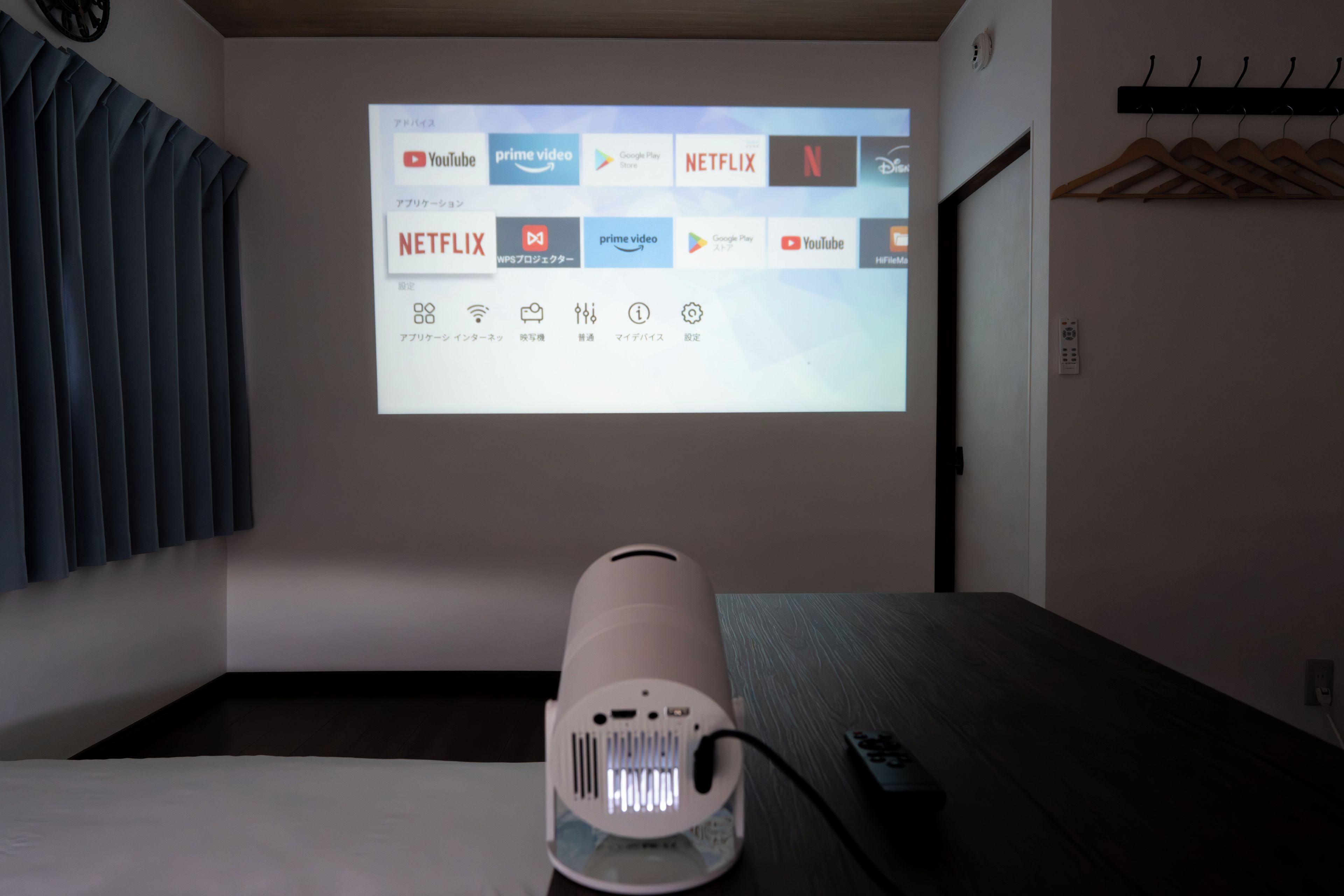 Eine Projektion von Streaming-Diensten an einer Wand in einem Zimmer mit einem Bett, einer Fernbedienung und einer Wandheizung.