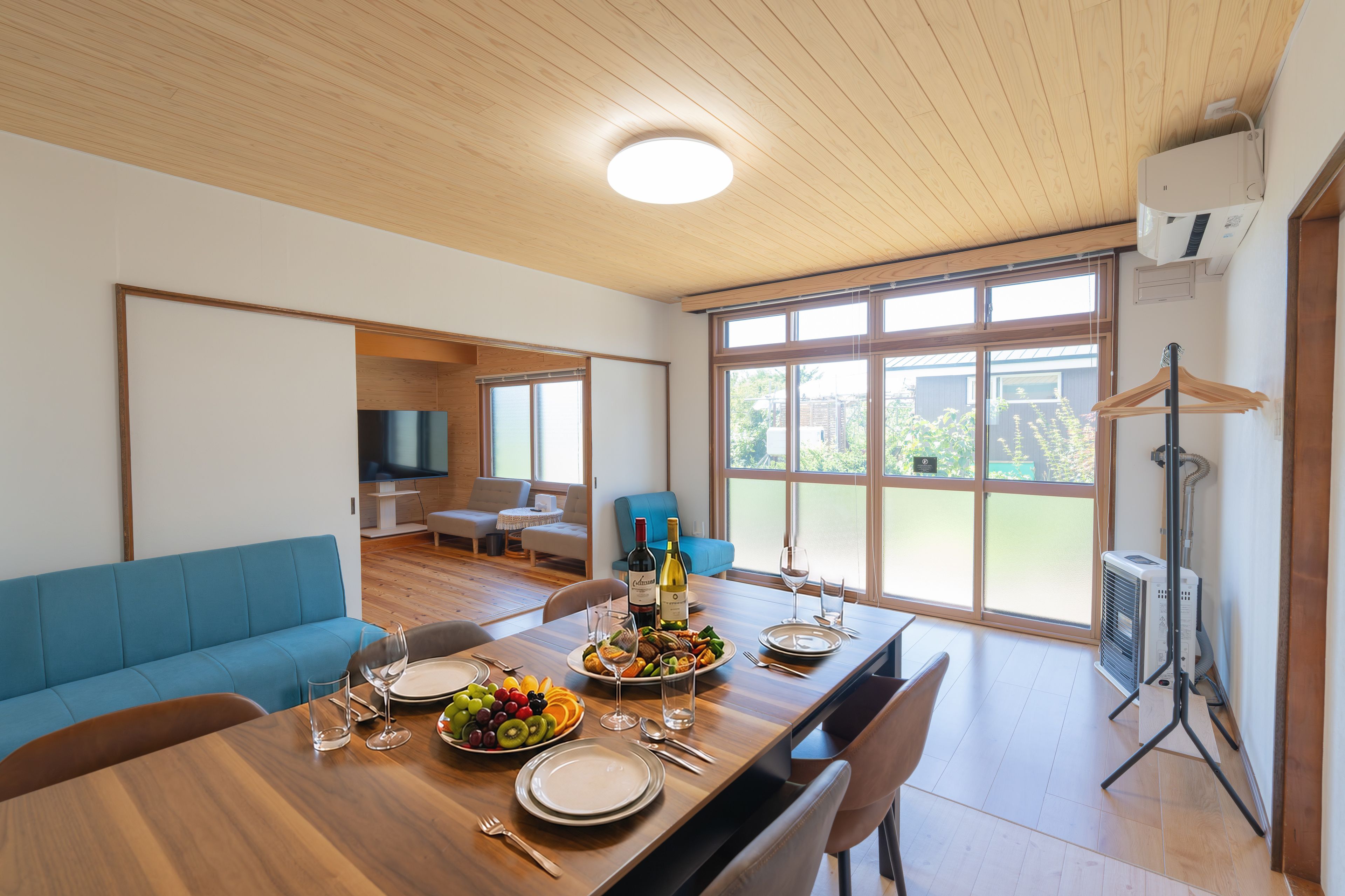 A dining area with a wooden table set for a meal, a blue sofa, and a large window with a view of greenery.