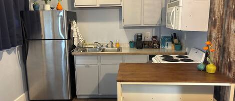 A compact kitchen with a refrigerator, stove, microwave, and a wooden island with stools.