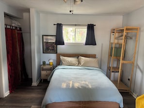 A bedroom with a bed, a nightstand, a window with curtains, a wooden ladder, and a wardrobe.