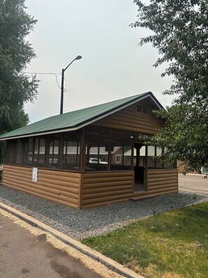 A wooden cabin with a green roof, large windows, and a gravel driveway.