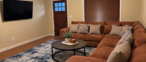 Ein Wohnzimmer mit einem Ecksofa, einem Couchtisch, einem Flachbildfernseher, einem Deckenventilator und einer Tür mit Fenster.