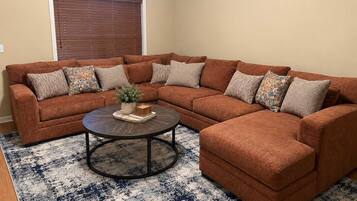 A sectional sofa with multiple cushions, a coffee table, and a patterned rug in a living room.