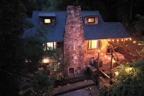 Ein Steinhäuschen mit Schornstein, einer Holzterrasse und Lichterketten.