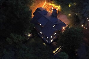Ein zweistöckiges Haus mit dunklem Dach, umgeben von Bäumen und einem kleinen Garten mit Beleuchtung.