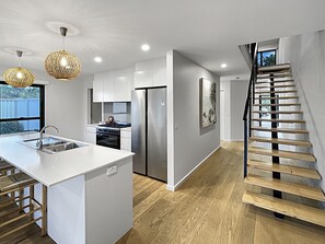 Cozinha moderna com ilha central, eletrodomésticos de aço inoxidável e escada de madeira.