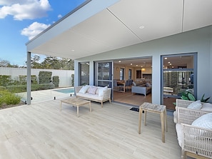 Un espace de vie extérieur moderne, doté d’une piscine, d’un patio couvert et offrant une vue sur l’intérieur de la maison.