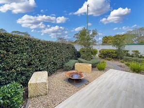 A landscaped outdoor area with a wooden deck, a fire pit, and various shrubs.
