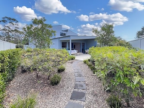 A modern house with a covered patio, a stone pathway leading to the entrance, and a well-maintained garden.