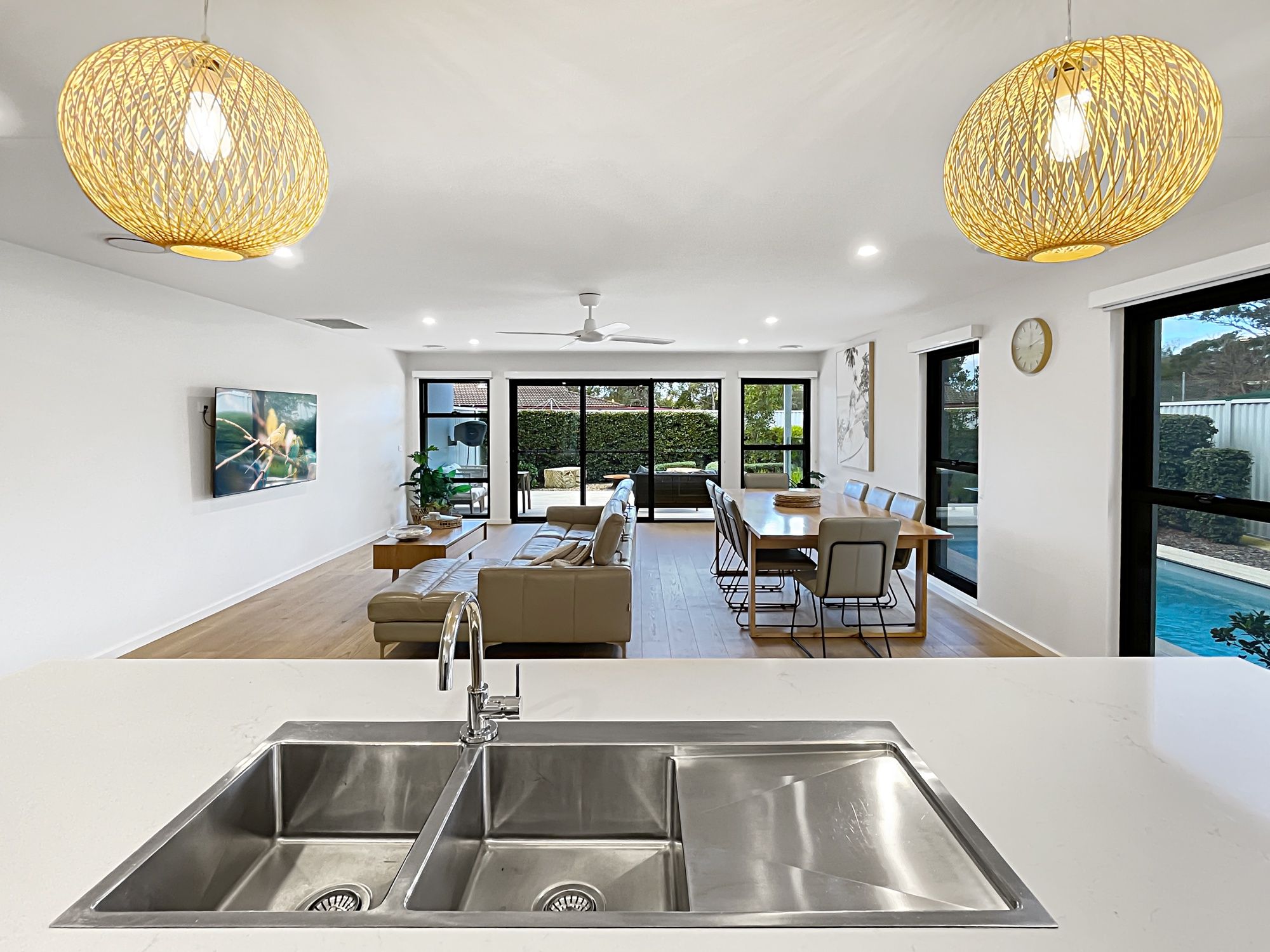 A modern kitchen with a large sink, dining area with a table and chairs, and a view of a swimming pool.